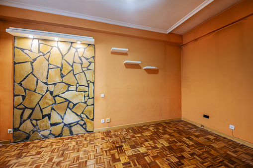 Empty room with peach colored walls, absurd stonework on the wall, oak joinery and checkerboard style plank parquet floors