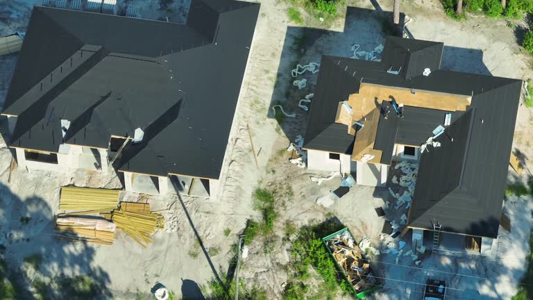 Aerial view of workers working on residential private home covering wooden roof with asphalt shingles. House under construction in Florida quiet rural area. Real estate development concept