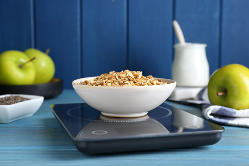 Electronic scales with granola on light blue wooden table