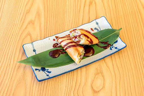 Delicious Asian crispy roll stuffed with vegetables on banana leaf and red sauce on wooden table