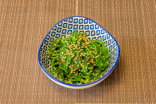 wakame seaweed salad with sesame and soy sauce inside a bowl with blue motifs and on a brown tablecloth