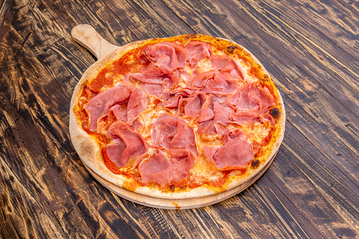 Italian prosciutto pizza with lots of ham and lots of melted mozzarella cheese and tomato