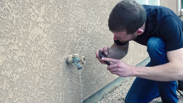 Young Male Home Inspector Taking Smart Phone Photo of Outdoor Water Faucet on a Stucco Home