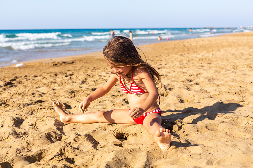 Little girl sitting in the sand on the beach and playing