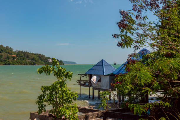 Slightly rickety stilt bungalows with blue pyramid roofs on the Phuket coast facing the Andaman Sea on a summer day.