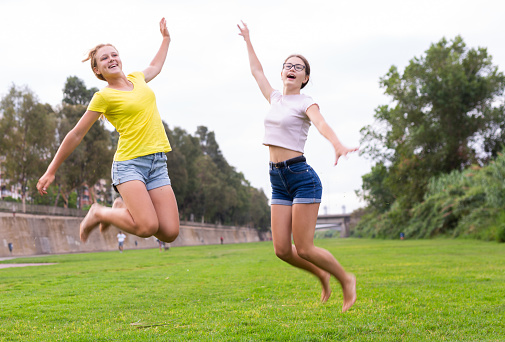 Two positive teenager girls jumping on field in summertime.