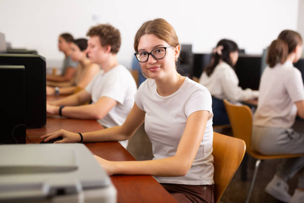 istock Positive female teenager in glasses learning computer science while she is using a PC in the computer classroom 1485869692
