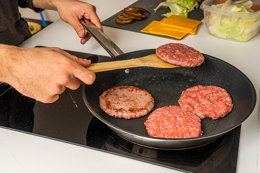Cooking several beef burgers on an electric griddle by the hands of a young man