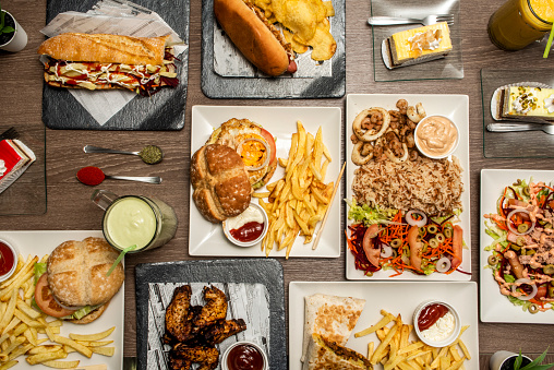 Fast food dishes with basmati rice with squid, hot dogs, assorted burgers, sandwich with sauce and fries, desserts and cakes, barbecue wings