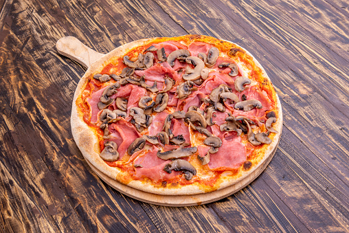 whimsical italian pizza recipe with prosciutto, mushrooms and tomatoes on wooden table