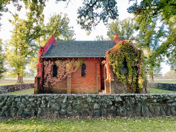 Horizontal landscape photo of the All Saints Anglican Church or Gostwyck Chapel, popular historic tourist site, surrounded by a low stone wall and Elm and Oak trees, located on Gostwyck Station in the New England high country near Armidale, NSW