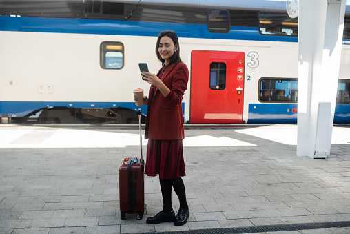 Beautiful Asian businesswoman on a journey waiting at the train station and using smartphone