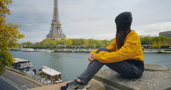 Tourist women wearing yellow shirt enjoying great view on the Eiffel tower sitting on the bridge, background of the Eiffel Tower in Paris.