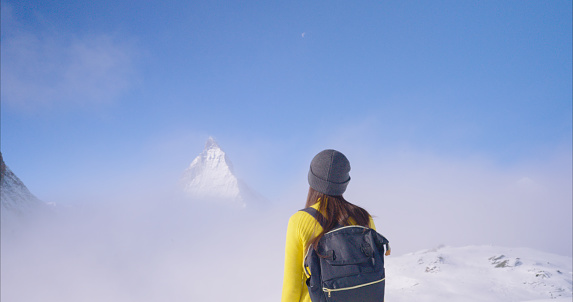 Rear view of young woman wearing yellow shirt with backpack standing on top summit of view Matterhorn mountain in Switzerland.