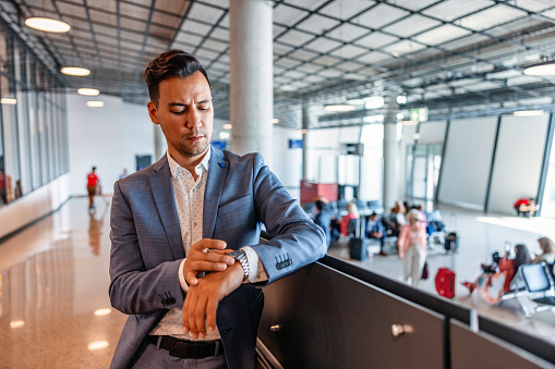 A Japanese businessman, smartly dressed in a business suit, checking the time while waiting for his next business trip at the airport.