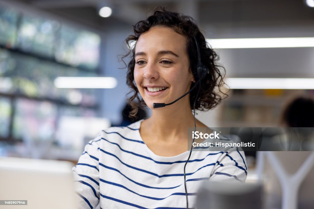 Customer service representative using a headset while working at a call center Happy Latin American customer service representative using a headset while working at a call center Call Center Stock Photo