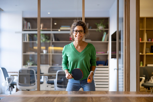 Happy Latin American woman playing ping pong on an active break at the office