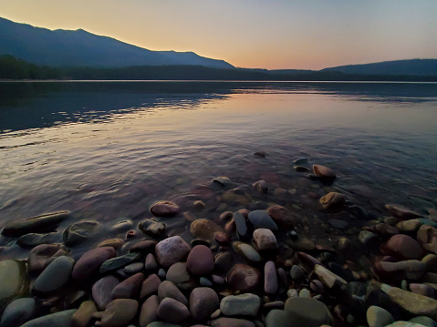 This is a photograph taken on a mobile phone outdoors at dusk of the rocky shore of Lake MacDonald in Glacier National Park, Montana during autumn of 2020.