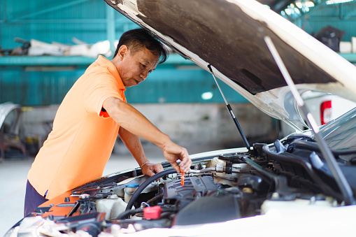 Senior Asian man checking or measuring a vehicle oil engine or engine lubricant level by using oil stick indicator. Senior professional repairman inspecting an oil engine in an old car.
