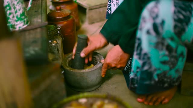 Colse Up of Man Hand Grinding Spices for Herbal Drink with Pestle and Mortar in Traditional Javanese Clothing