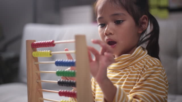 A young cute Asian girl is using the abacus with colored beads to learn how to count at home