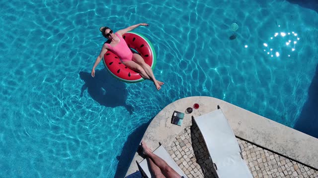 Birds eye view of woman laying on inflatable donut in clear blue pool water