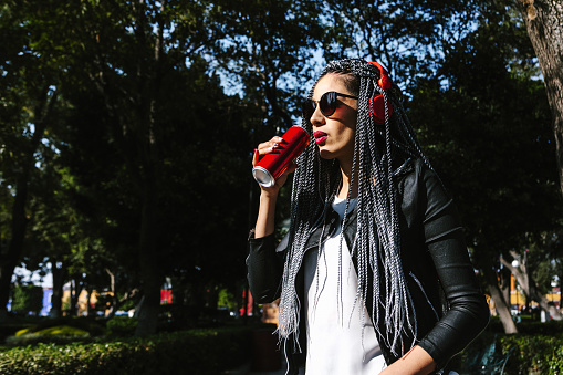 Young latin woman with braids hair holding beverage drink soda can on the street in Mexico, hispanic people