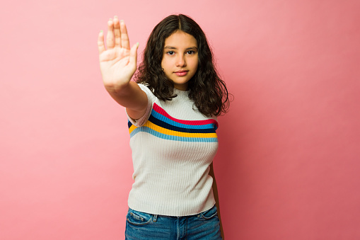Angry mexican teen girl looking upset while showing her palm and asking to stop bullying and violence