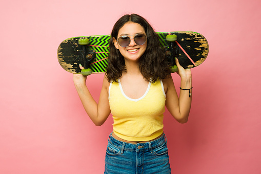 Portrait of a happy teen girl wearing retro vintage sunglasses ready to enjoy skating using a skateboard