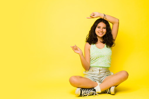 Fun thirteen-year-old girl pointing to a yellow copy space ad while sitting looking happy in the studio