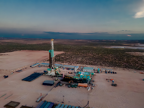 Stunning drone view captures the orange and pink hues of a sunset over an oil rig in the Permian Basin, where fracking drilling operations are in progress