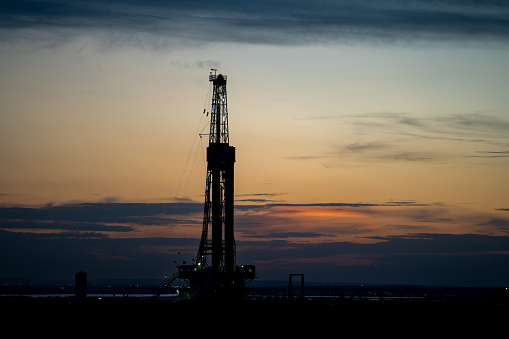 Drone view captures the Permian Basin at sunset, revealing the sprawling landscape of fracking drilling and oil rigs that stretch out towards the horizon