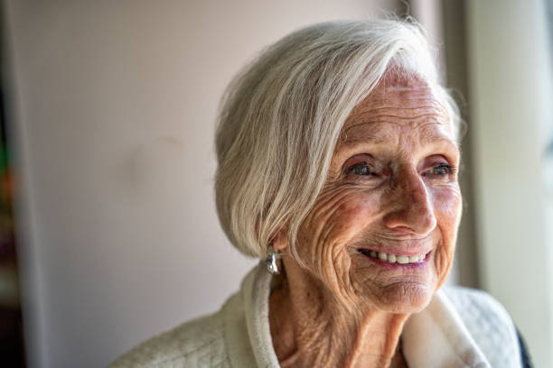 istock Elderly woman looks contentedly through a window while smiling at the camera, radiating a peaceful and joyful energy 1485935171