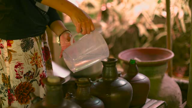 Close Up Woman Pourinng water From Plastic Jug to Traditional Terracotta Clay Container