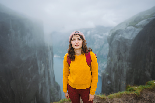 Cheerful woman in yellow sweater with backpack hiking one the background of Lyserfjord