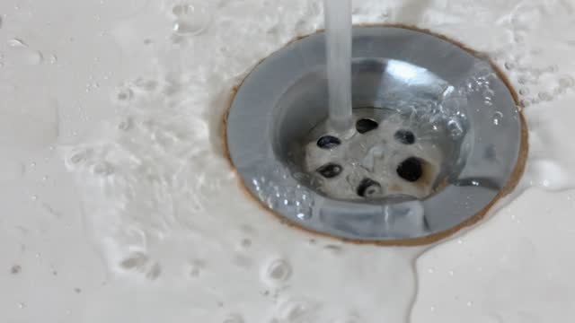 Water drain in ceramic sink hole. Stream of water going down into sink drain, close up