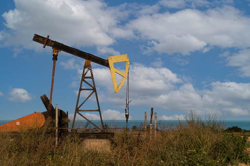 A small oil pump, an energy industrial oil machine, in the agricultural field in Bulgaria. In the background is the Black Sea