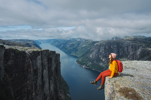 Woman in yellow sweater  sitting on the cliff above Lysefjorden