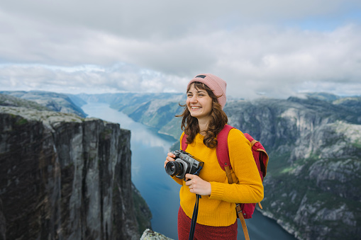 Woman  in yellow and red outfit photographing  Lysefjorden from Kjerag mountain