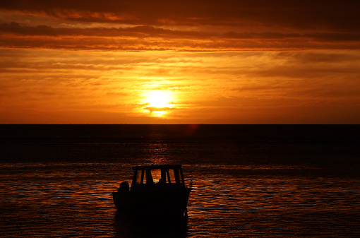 Albion, Mauritius - April 27, 2023: Dark clouds and vibrant colors during sunset at the Indian Ocean close the public beach of Albion in the West of Mauritius. Silhouette of a fisherman boat.