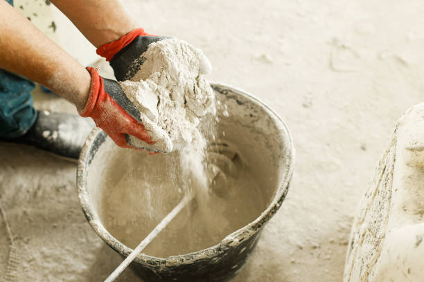 Worker mixing gypsum plaster with water for plastering walls. Construction of house and home renovation concept. Close up of bucket with stucco mix and handyman hands stock photo