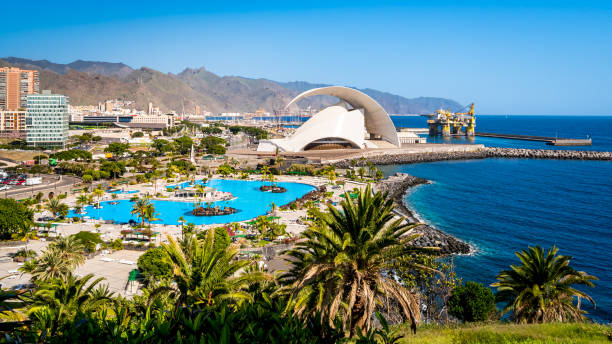 santa cruz de tenerife avec l’emblématique salle de concert auditorio de tenerife qui brille au soleil sur fond de montagnes anaga, d’une plate-forme pétrolière et d’une piscine tropicale avec des palmiers au premier plan. - tenerife spain santa cruz de tenerife canary islands photos et images de collection