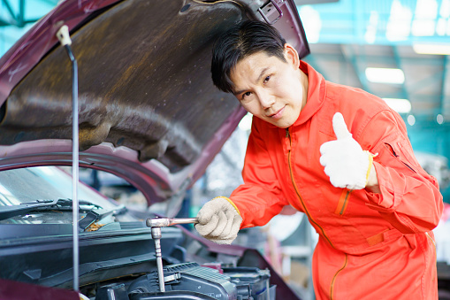 Automobile technician working in auto garage, technician holding a wrench preparing to repair broken vehicle. Professional auto or car repairman fixing a crashed car.