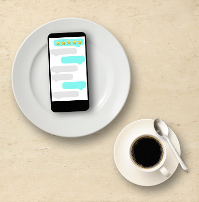Close-up of smartphone with reviews evaluation on five star rating on a white plate, on a marble table with coffee.
Customer feedback concept