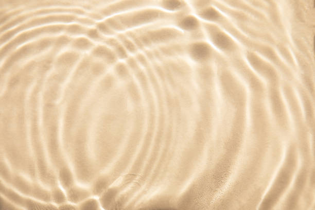 Abstract nature textured background, water waves in the pool with sun reflection. Clear water with bubbles and circles on beige background