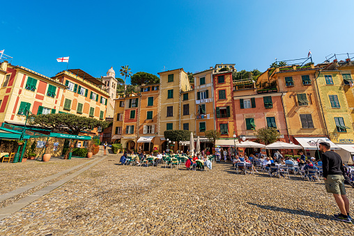 Portofino, Liguria, Italy - April 8th, 2023: Group of tourists in in the famous village of Portofino on a sunny spring day, luxury tourist resort in Genoa Province, Liguria, Italy, Europe. The village of Portofino is a famous vacation resort of the Liguria for its picturesque harbor and colorful houses that are reflected in the sea. In ancient times it was a small fishing village. Many celebrity and artists frequent this Italian seaside resort.