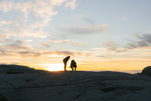 Silhouette of man and woman standing on the hill and looking at sunset