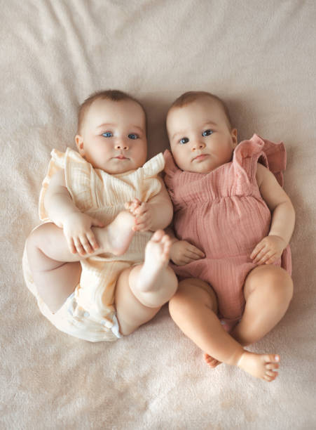 foto vetica di due sorelle bambine in vestiti di cotone simili sdraiate sul letto. gemelli fraterni . - twin newborn baby baby girls foto e immagini stock