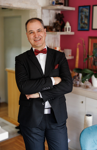 Portrait of handsome mature man in suit standing and looking at camera at home