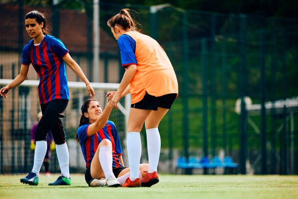 Soccer player assisting her teammate in getting up after a foul on playing field. Female player helping her teammate to get up on soccer pitch. Copy space. foul stock pictures, royalty-free photos & images